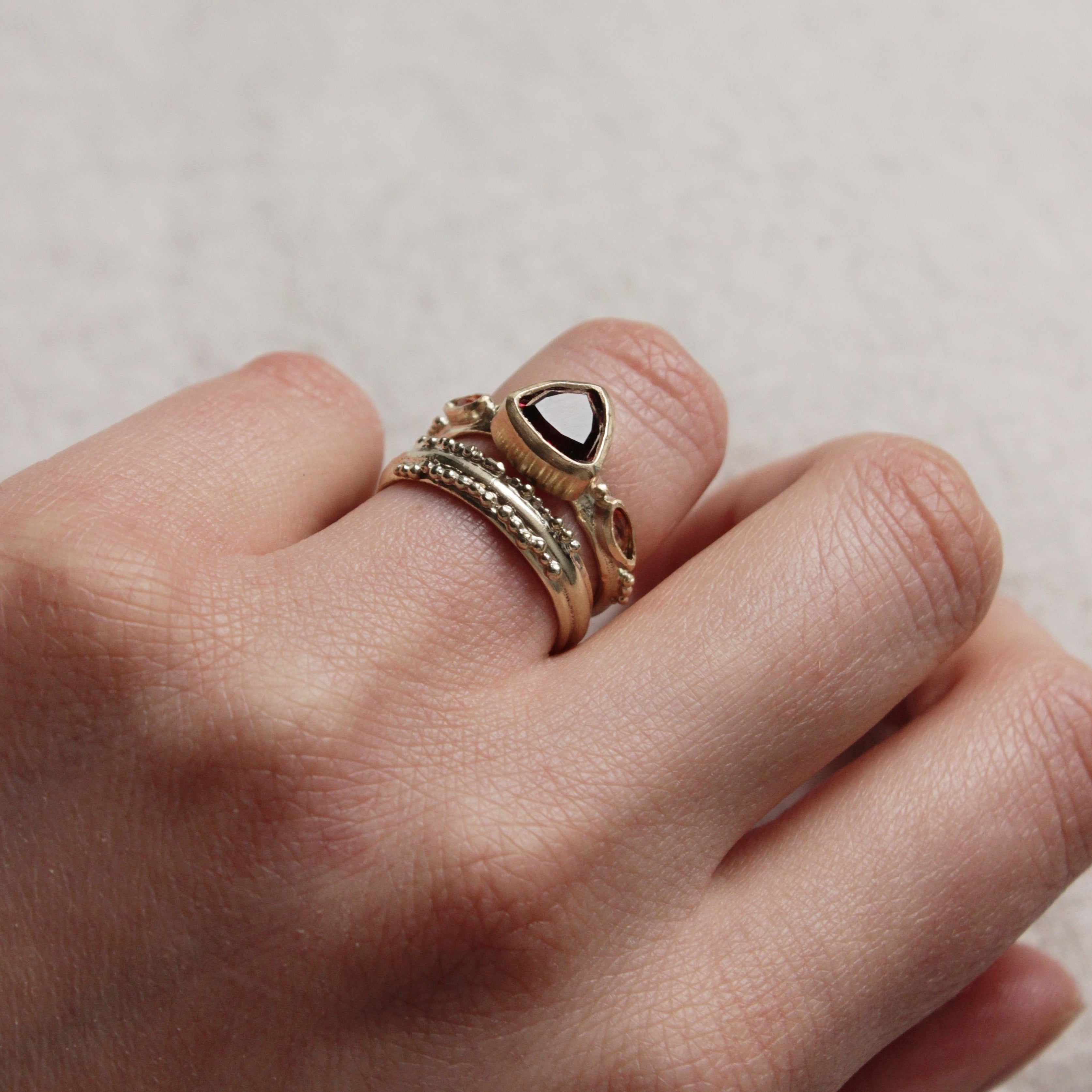 Alternative pink tourmaline engagement ring, handcrafted by Josie Mitchell jewellery in Frome, Somerset. Featuring a stunning deep pink tourmaline stone with peach coloured sapphires on either side and delicate gold granules. Worn with the Ancient wedding band.