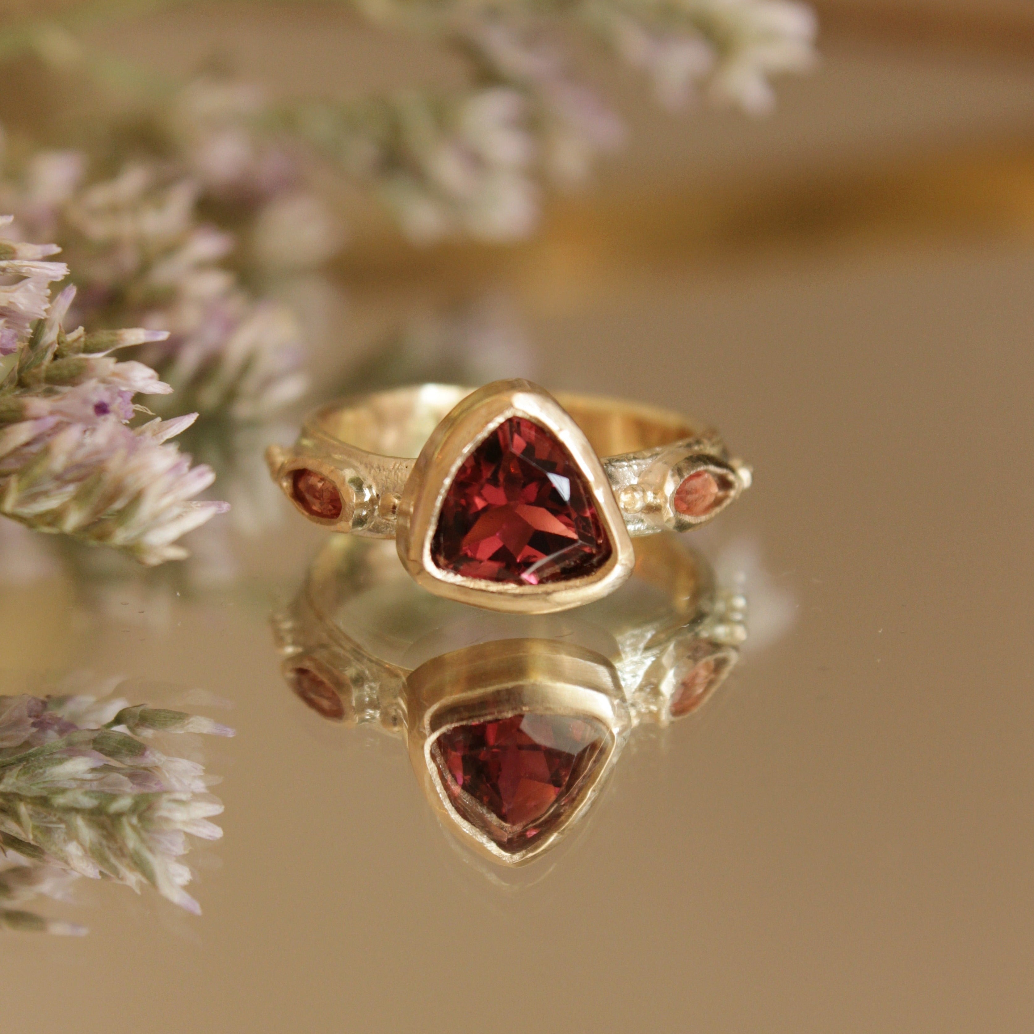 Alternative pink tourmaline engagement ring, handcrafted by Josie Mitchell jewellery in Frome, Somerset. Featuring a stunning deep pink tourmaline stone with peach coloured sapphires on either side and delicate gold granules.